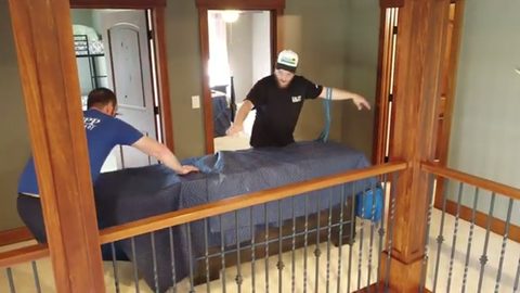 two movers blanket-wrapping a bedroom set on a stair landing, face visible