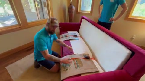 mover securing furniture padding on a red sofa arm, face visible