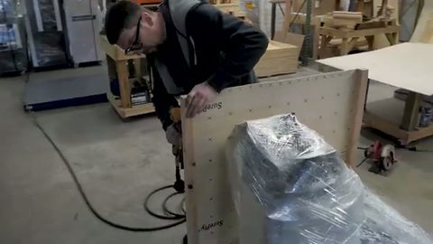 worker screwing plywood panels together to build a shipping crate, face visible