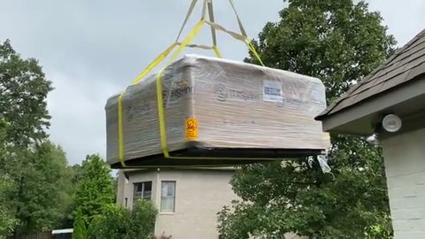 wrapped hot tub lifted on crane straps beside a house