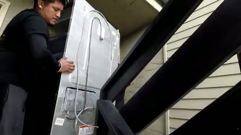 mover carrying a refrigerator up wooden exterior stairs, face visible