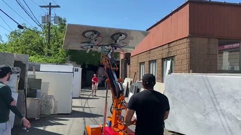 worker moving a marble slab with a powered vacuum lifter at a stone yard