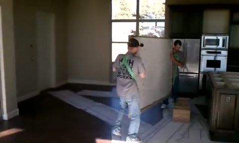 two movers maneuver a stone countertop slab past kitchen appliances, face visible