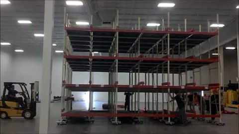 movers relocating a multi-level pallet rack on dollies with a forklift