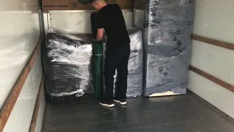 mover securing shrink-wrapped furniture inside a moving truck